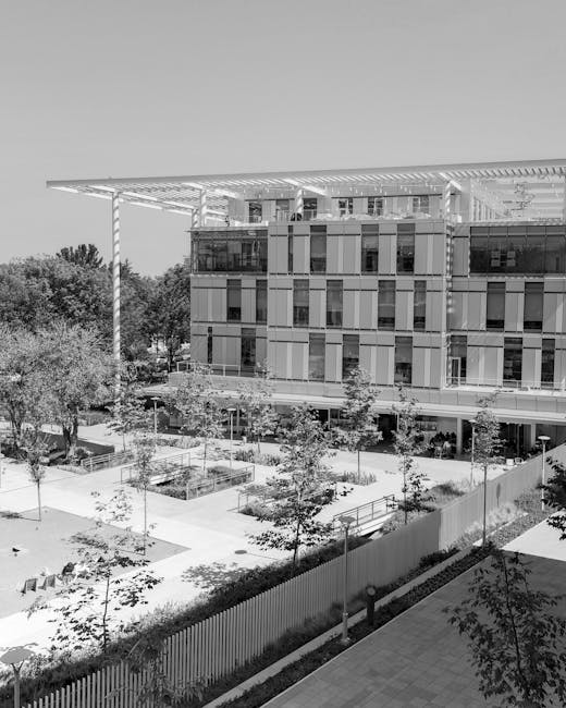 A modern multi-story building on the Brunel University campus in Uxbridge, featuring large glass windows and a prominent overhanging roof supported by sleek columns. In the foreground, there is a well